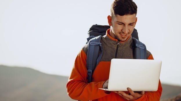 a boy using laptop when he is traveling and a blue backpack in his shoulder