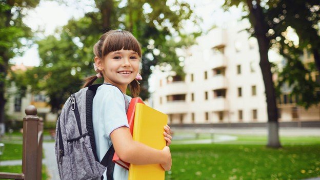 a schoolgirl holding two books in her hands and a backpack in her shoulder