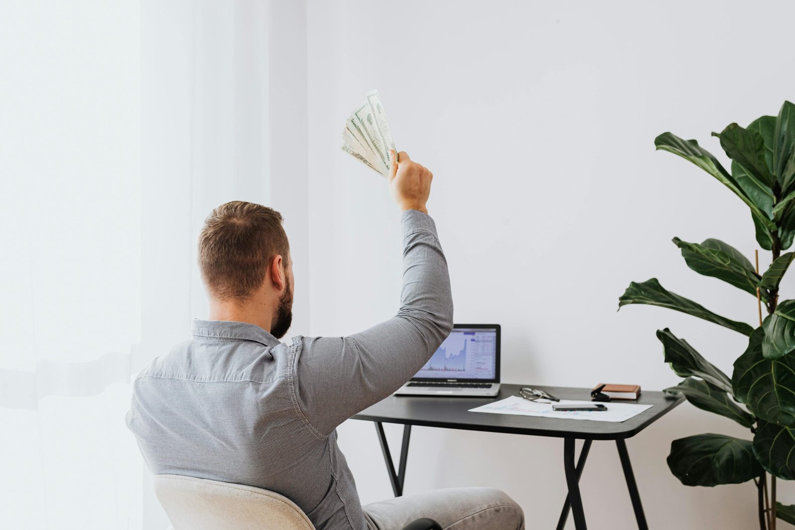 A man in a home office raises cash, symbolizing financial success and achievement.